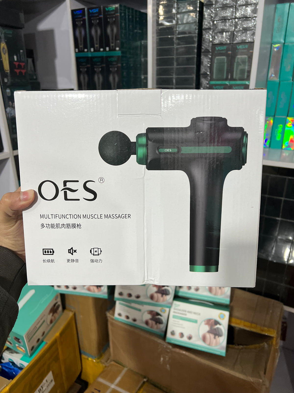 OES massage gun packaging held in front of a cluttered background