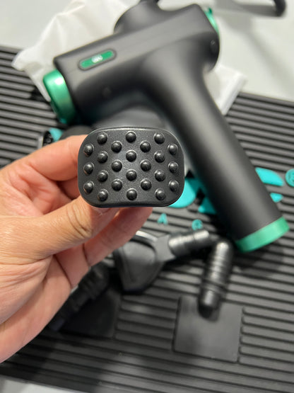 Black and green grooming tool with a textured black pad held by a hand against a blurred background.