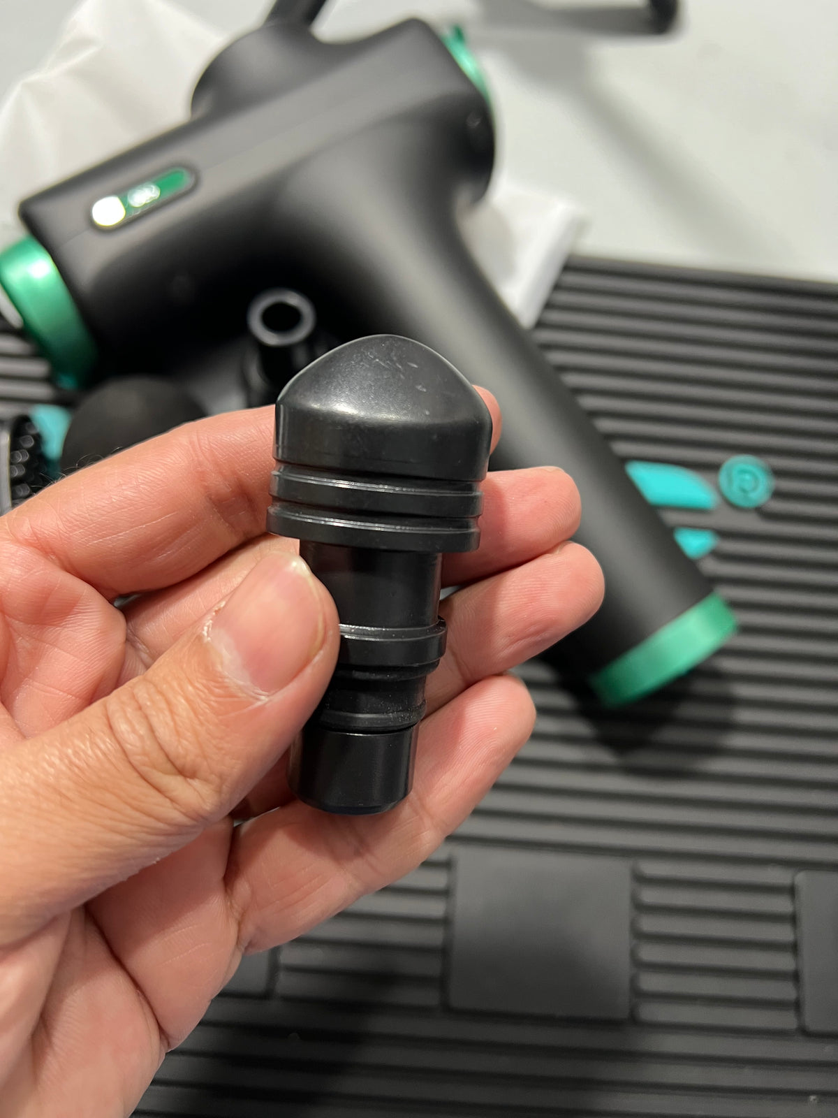 Hand holding a black nozzle against a blurred background with a vacuum cleaner.
