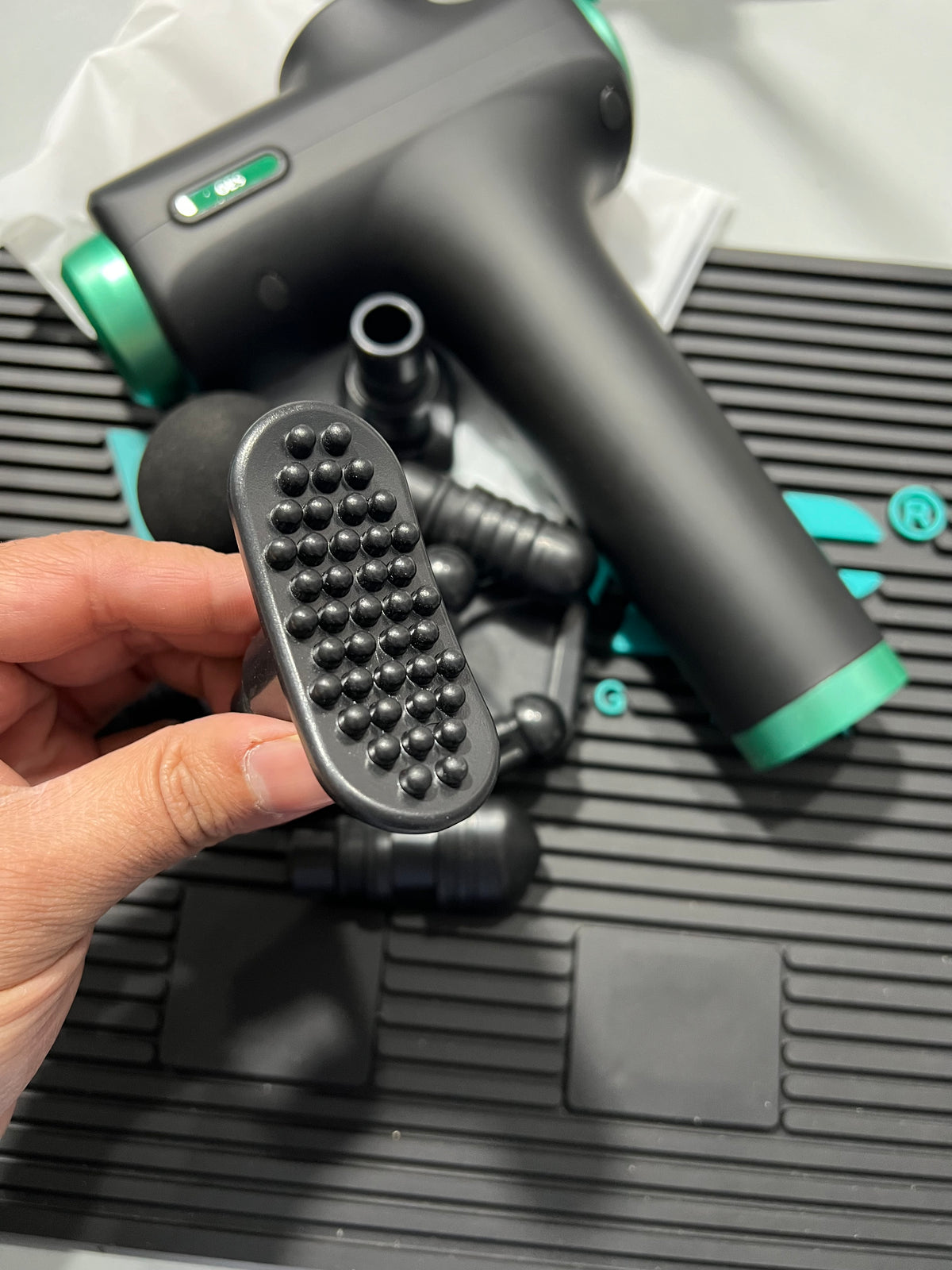 Hand holding a black and green garden tool with a textured foot plate against a blurred background
